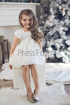 5 years old little girl dressed in beautiful fashion white flower dress posing near Christmas tree