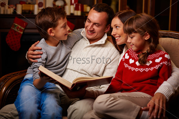 Modern family of father, mother, son and daughter reading together, stock photo