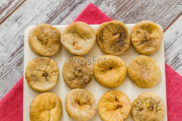 Dried figs in plate on pink napkin and white wooden background