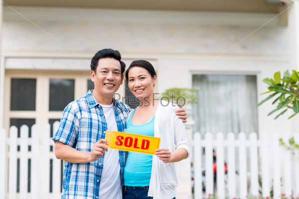 Happy Asian middle-aged couple holding sold sign