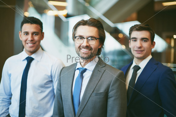 Happy mature boss looking at camera with two employees on background