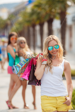 Happy shopping woman with a group of friends at the background. shopping and tourism concept - beautiful girls with shopping bags in citiy.