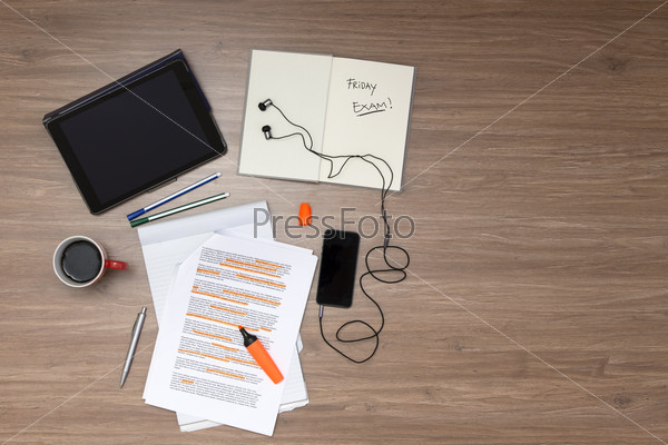 Background, filled with studying materials and copy space on a wooden surface. Items include an electronic tablet,  cup of coffee, pens, markers, a high lighted standard (lorum ipsum) text