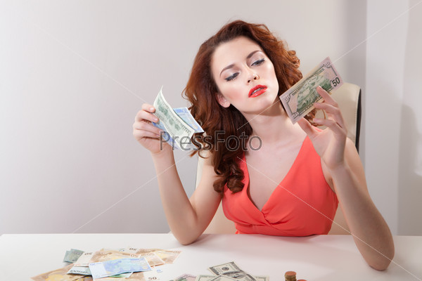 a young girl at  table with greedy counts  money lying on table and looking at  camera