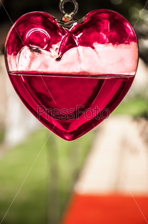 A glass heart with red liquid hanging from the ceiling with the walkway in the background.