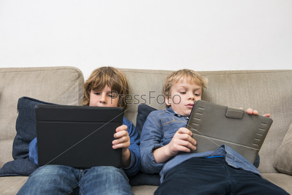 Boys Using Digital Tablets On Sofa