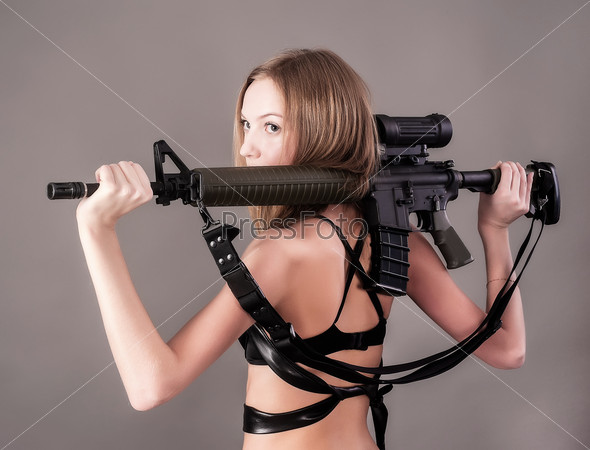 Beautiful sexy blond woman holding army rifle over grey background