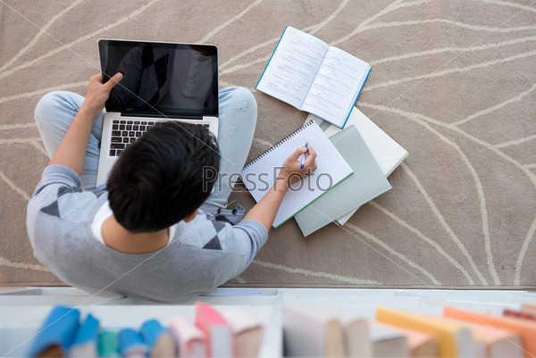 Student sitting on the floor with a laptop and doing homework, view from above