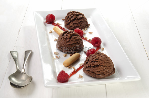chocolate ice cream with fruit sauce, raspberries and chocolate curls on a white plate