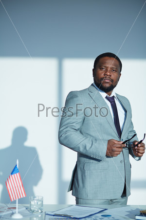Calm businessman in suit standing by his workplace