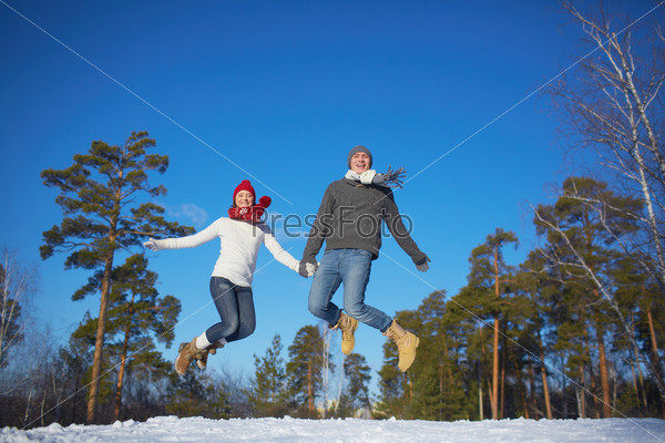 Joyful dates in knitted clothes jumping in winter park or forest