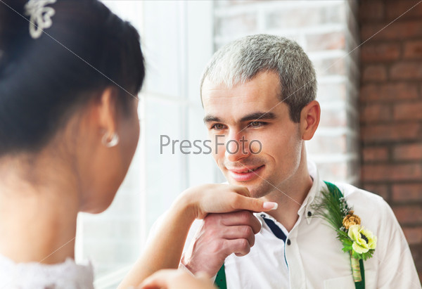 Cheerful married couple standing near the brick wall. Focus on groom