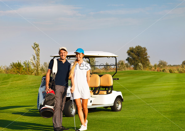 Young sportive couple playing golf on a golf course. Standing near the golfcar