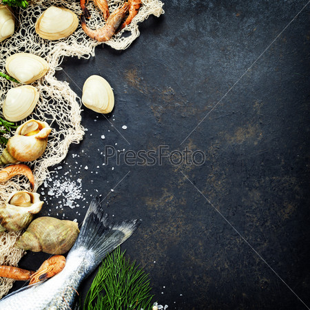 Delicious fresh fish and seafood on dark vintage background. Fish, clams and shrimps with aromatic herbs, spices and vegetables