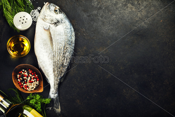 Delicious fresh fish on dark vintage background. Fish with aromatic herbs, spices and vegetables - healthy food, diet or cooking concept