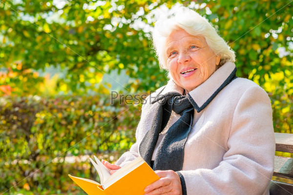 Elderly woman with a book resting on a bench, stock photo