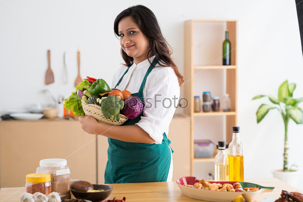 Portrait of Indian woman with fresh vegetables standing in a kitchen