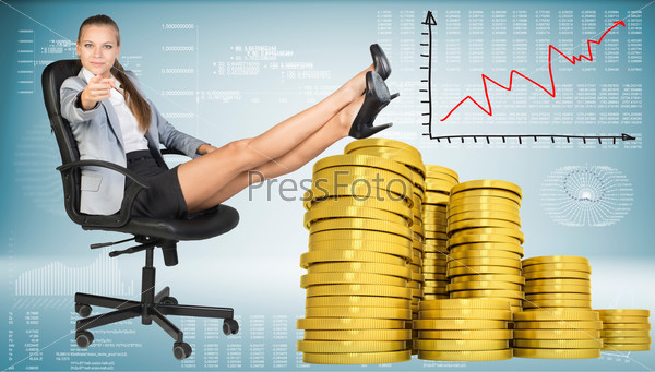 Businesswoman sitting on office chair with her feet up on piles of golden coins, pointing finger at camera. Graph showing growth beside. Hi-tech charts with various data as backdrop