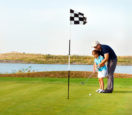 Father teaching daughter to play golf on putting on green