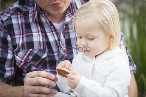 Adorable Little Girl Eating a Cookie with Daddy Outside.