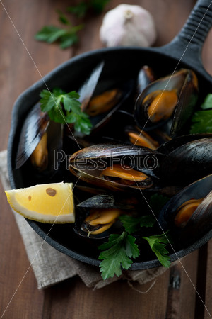 Close-up of steamed mussels with parsley and lemon in a frying pan, selective focus