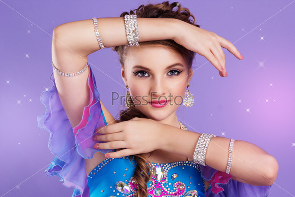 Portrait of beautiful belly dancer girl with nice makeup and heardress is wearing a colorful fashion costume. Isolated on purple