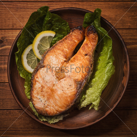 Baked trout steak in pottery with salad and slices of lemon, top view