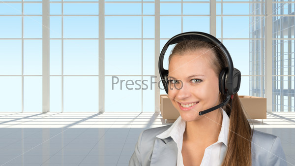 Businesswoman in headset, in vast white interior with transparent wall, looking at camera, smiling