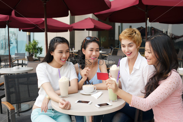 Young Vietnamese woman showing gift card to her friends in a cafe