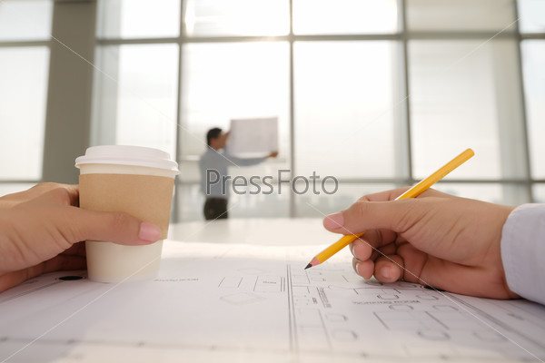 Hands of architect working on housing project and drinking coffee