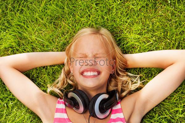 Laughing girl with headphones lays on green grass