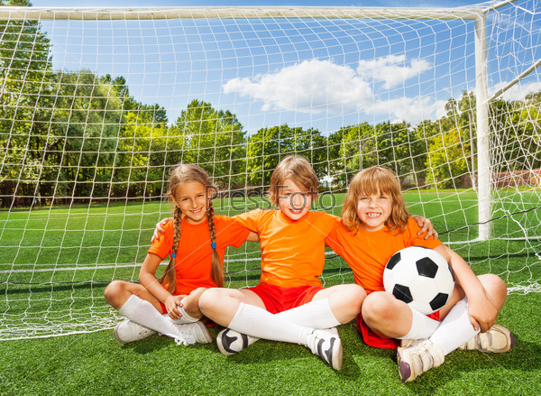 Smiling children sitting on grass with football
