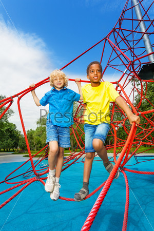Two boys stand together on red ropes of net