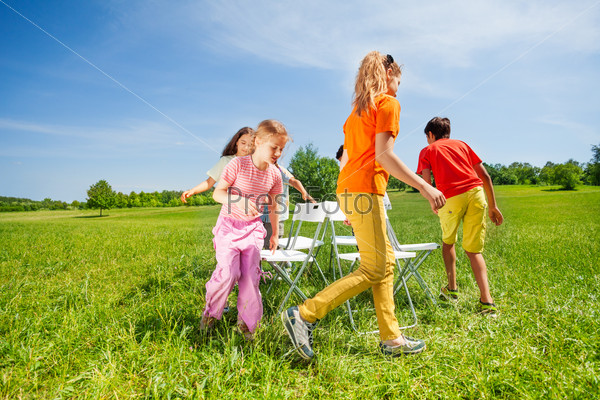 Children run around chairs playing a game outside in summer period, stock photo