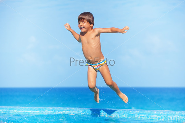 Happy boy jumps in water of swimming pool