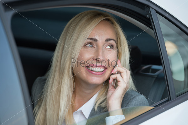 Attractive executive businesswoman sitting in car and calling by phone