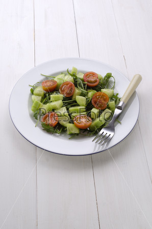 fresh vegetarian salad with cucumber, tomato and rocket salad on a white plate