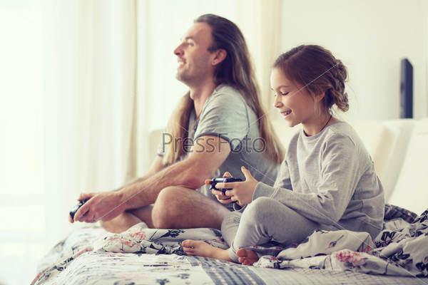 Child playing video game on tv with father in morning at bed at home