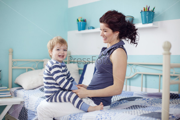 Young mother playing with her 2 years old little son at the bedroom