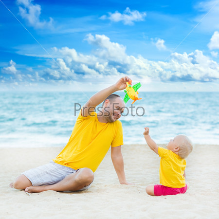 Baby and father on the tropical beach playing toy plane