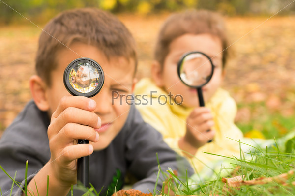 boy and girl look through a magnifying glass on the background of green grass and yellow leaves