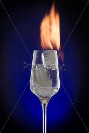 View of cocktail glass filled with burned ice on blue back
