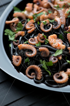 Squid ink tagliatelle with sliced octopus and parsley, close-up