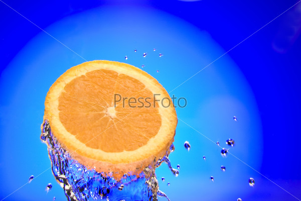 Close up view of sliced orange piece getting splashed with water, stock photo