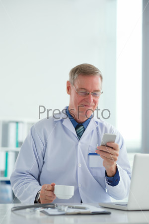 Male doctor drinking tea and messaging at break