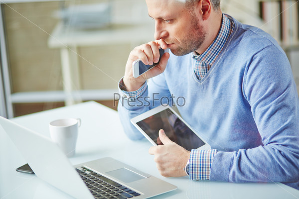 Pensive businessman working with multi-media gadgets in office