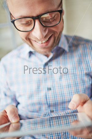 Smiling businessman in eyeglasses browsing in touchpad