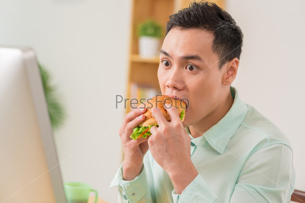 Man eating hamburger at stressful work
