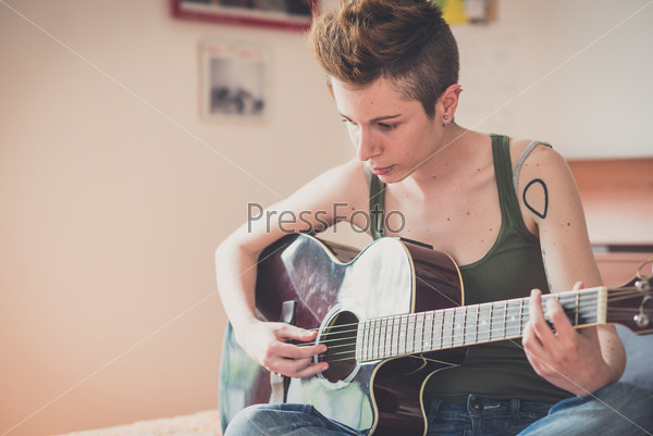 Young lesbian stylish hair style woman playing guitar at home , stock photo