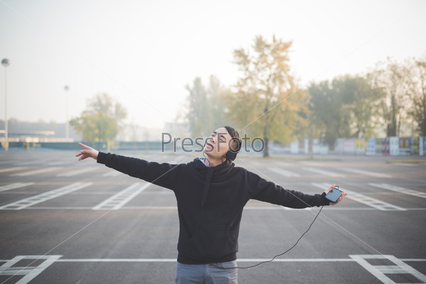 Young crazy funny asian man in town outdoor lifestyle listening music with headphones, stock photo
